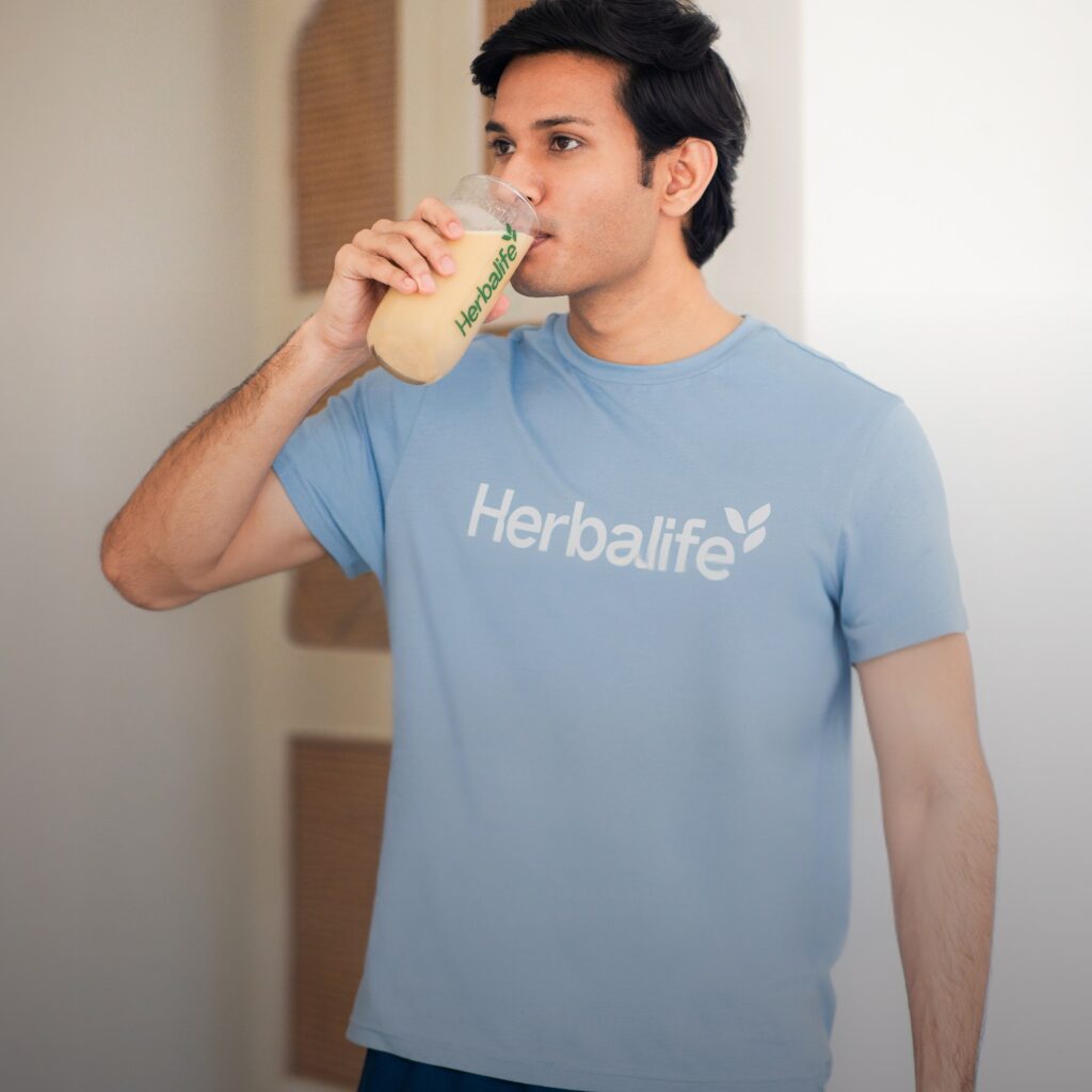 Homme en t-shirt bleu Herbalife buvant un shake protéiné pour une alimentation saine